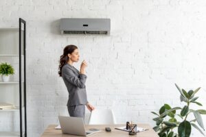 pretty businesswoman drinking water while standing near workplace under air conditioner
